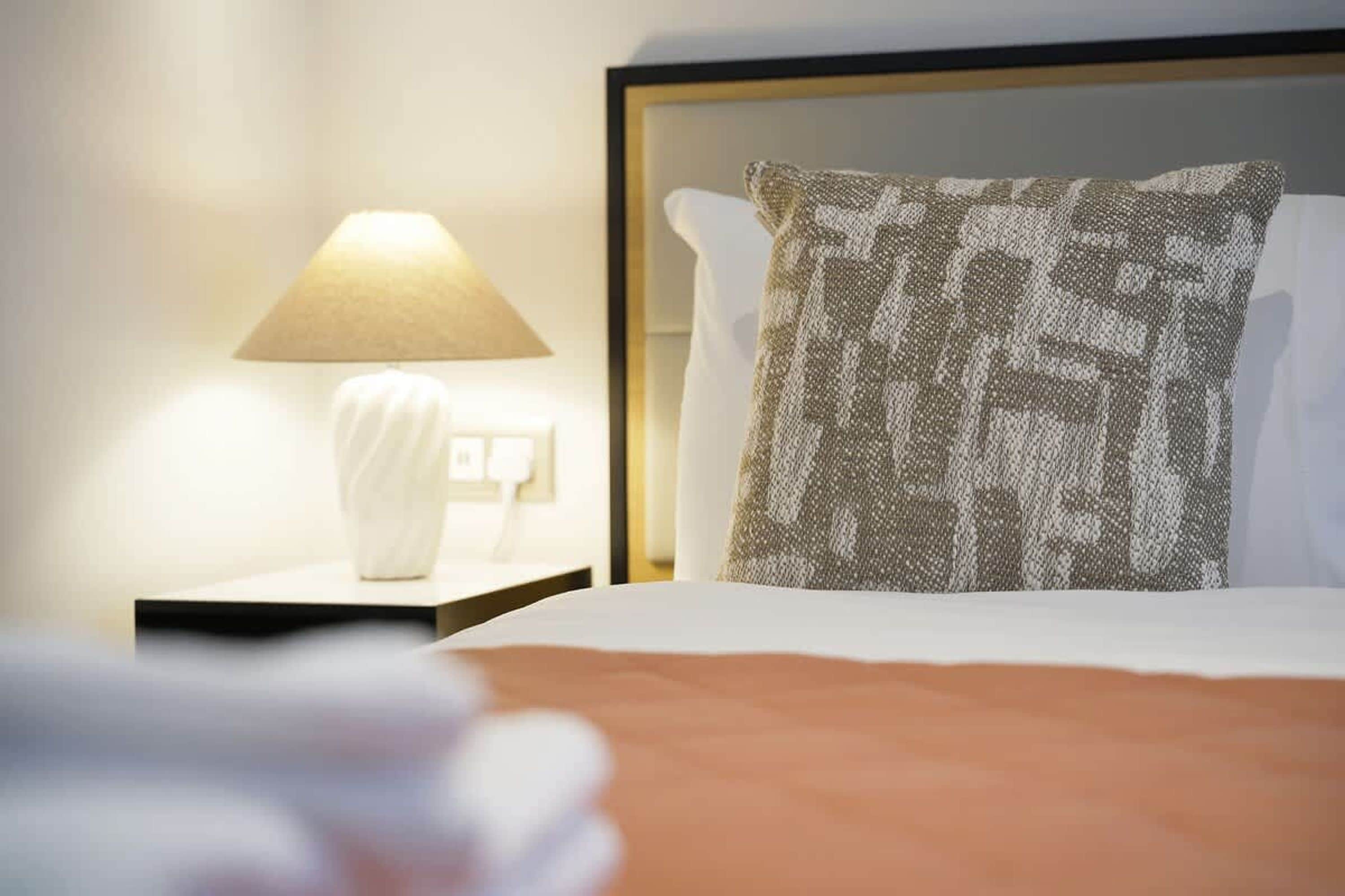 A neatly made bed with a patterned pillow and a bedside lamp on a nightstand.