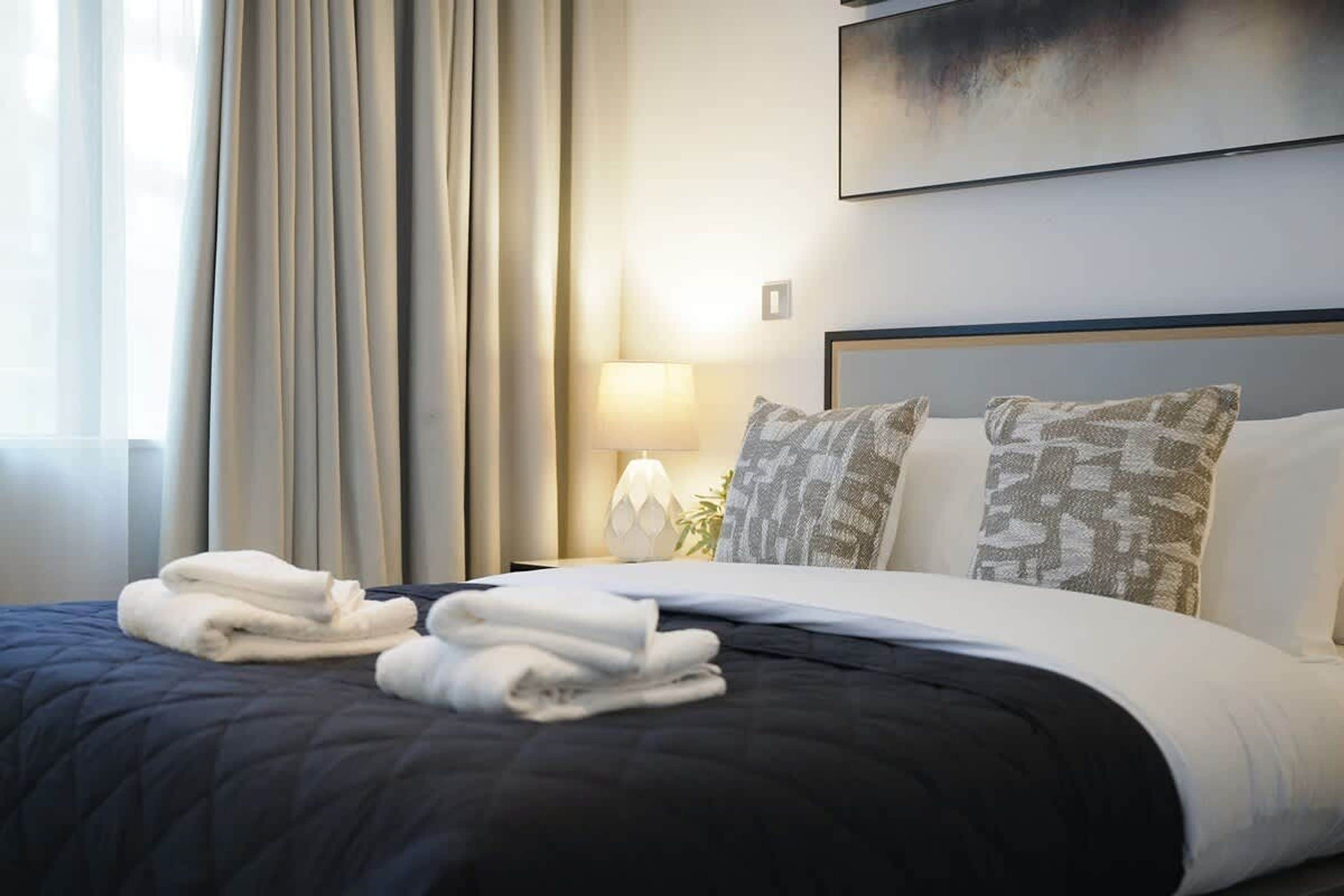 A hotel room with a bed, a nightstand, a lamp, and a view of the sea.