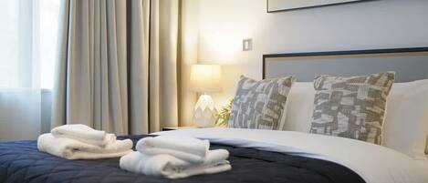 A hotel room with a bed, a nightstand, a lamp, and a view of the sea.