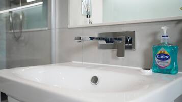 A bathroom with a white sink, a chrome faucet, and a bottle of Carex hand soap.