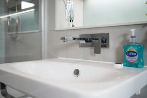 A bathroom with a white sink, a chrome faucet, and a bottle of Carex hand soap.