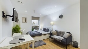 A modern bedroom with a bed, a sofa, a desk, and a TV mounted on the wall. - Perfect for Couples and Working Away in Manchester (Salford)