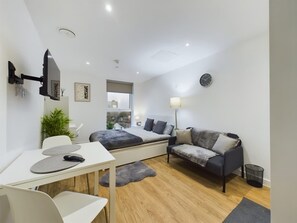 Ein modernes Schlafzimmer mit Bett, Sofa, Schreibtisch und einem an der Wand befestigten Fernseher.