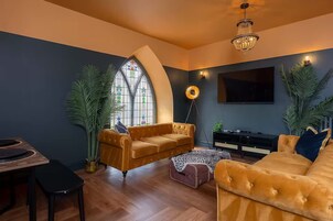 A modern living room with a large arched window, a hanging light fixture, and a flat-screen TV mounted on the wall.