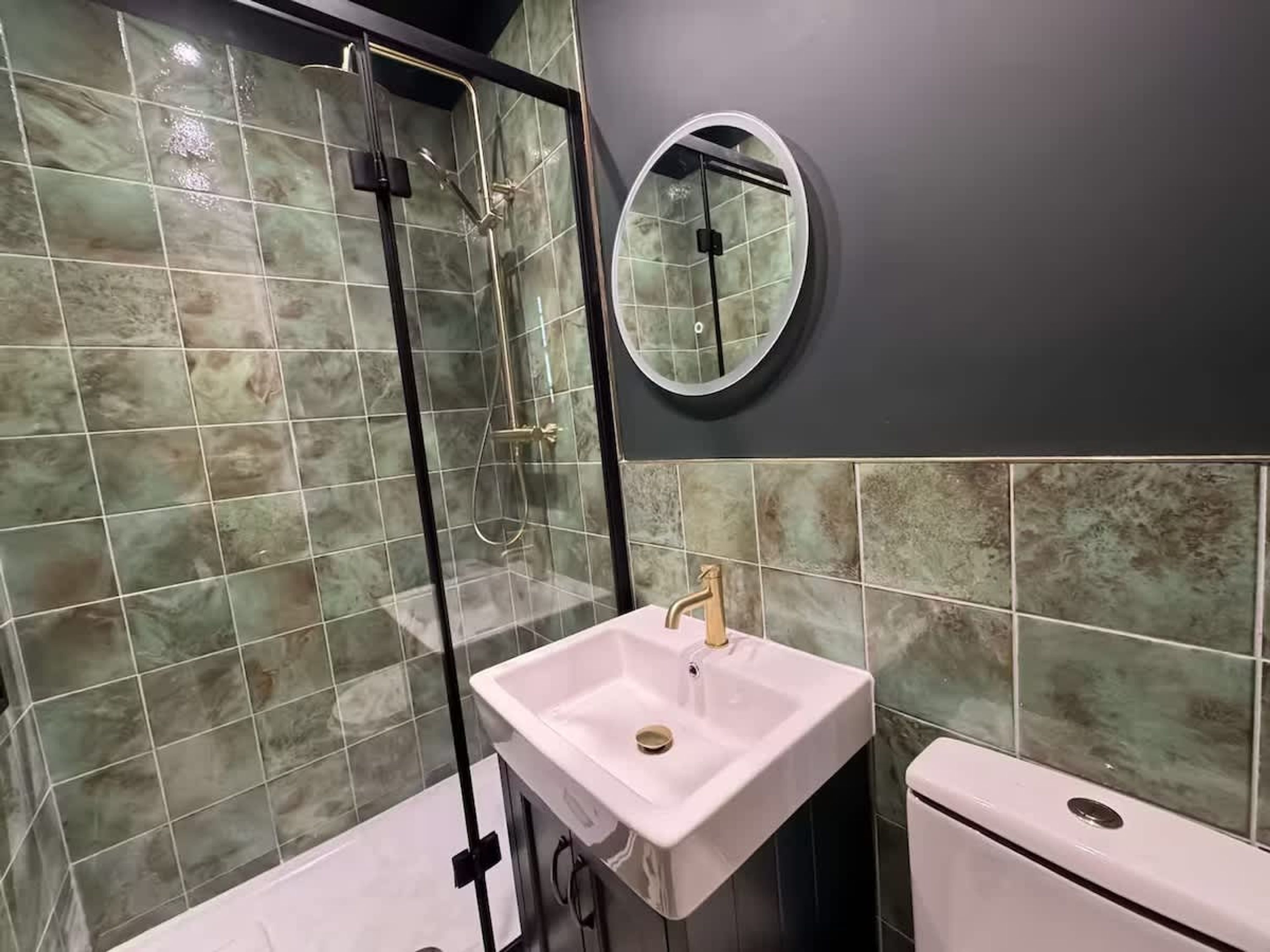 A bathroom with a glass-enclosed shower, a white sink, and a toilet.