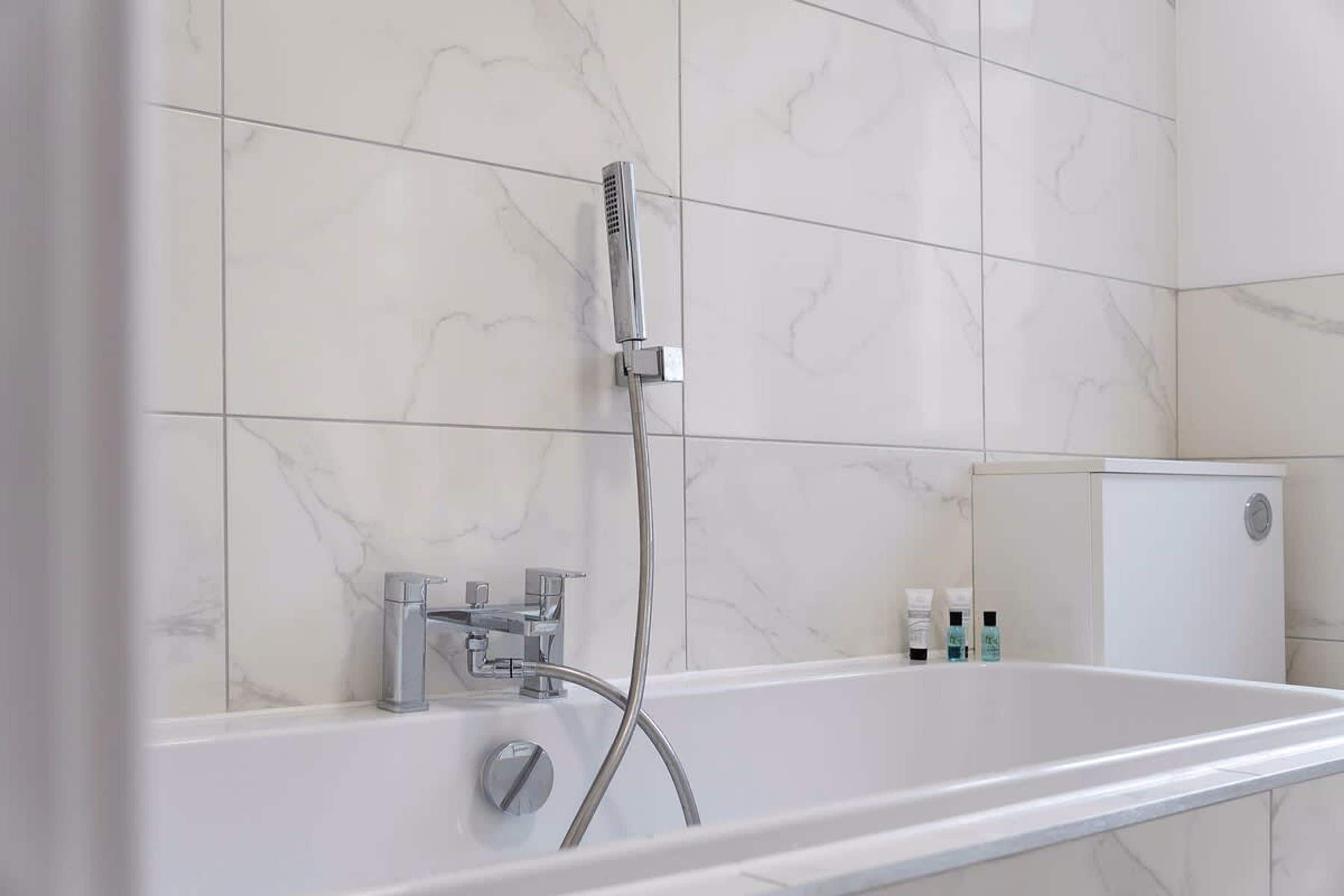 A modern bathroom with a freestanding bathtub, a handheld showerhead, and a wall-mounted faucet.