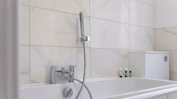 A modern bathroom with a freestanding bathtub, a handheld showerhead, and a wall-mounted faucet.