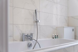 Un baño moderno con una bañera independiente, un cabezal de ducha manual y un grifo de pared.