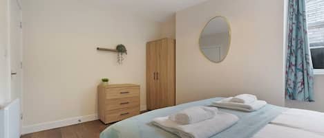 A bedroom with a bed, a dresser, a wardrobe, a mirror, and a window with curtains.