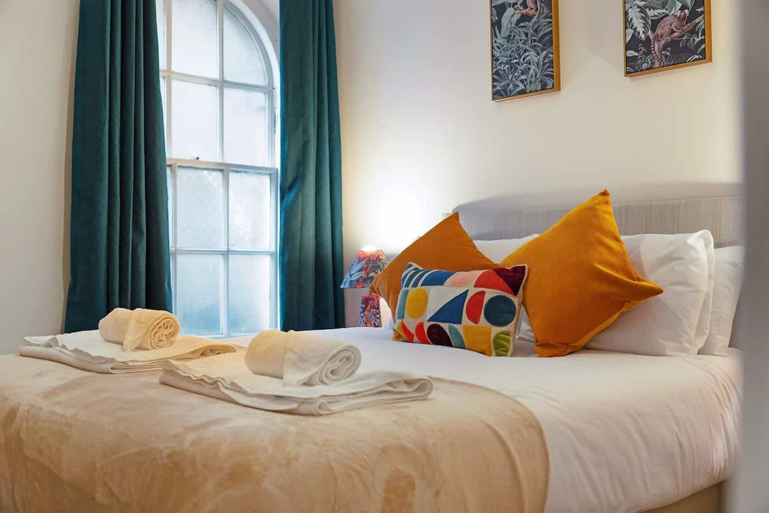 A hotel room with a neatly made bed, a window with curtains, and two wall-mounted paintings.