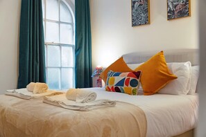 Habitación de hotel con una cama bien hecha, una ventana con cortinas y dos cuadros colgados en la pared.