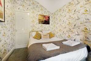 Een slaapkamer met een bed, kussens, een lijst met een foto en een deur.
