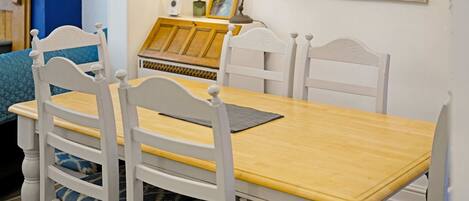 A dining table with four white chairs, a yellow tablecloth, and a framed picture on the wall.