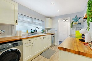 A modern kitchen with a built-in washing machine, a sink, and a countertop with various items. - Coastal 3-bed Home for Families Contractors (Redcar)