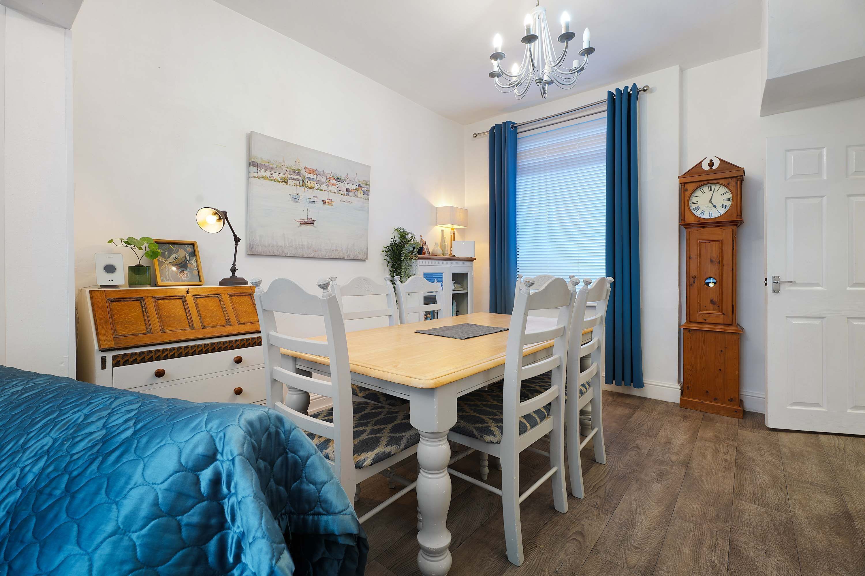 Une chambre à coucher avec un lit, un bureau, des chaises, une commode, une horloge et un tableau au mur.