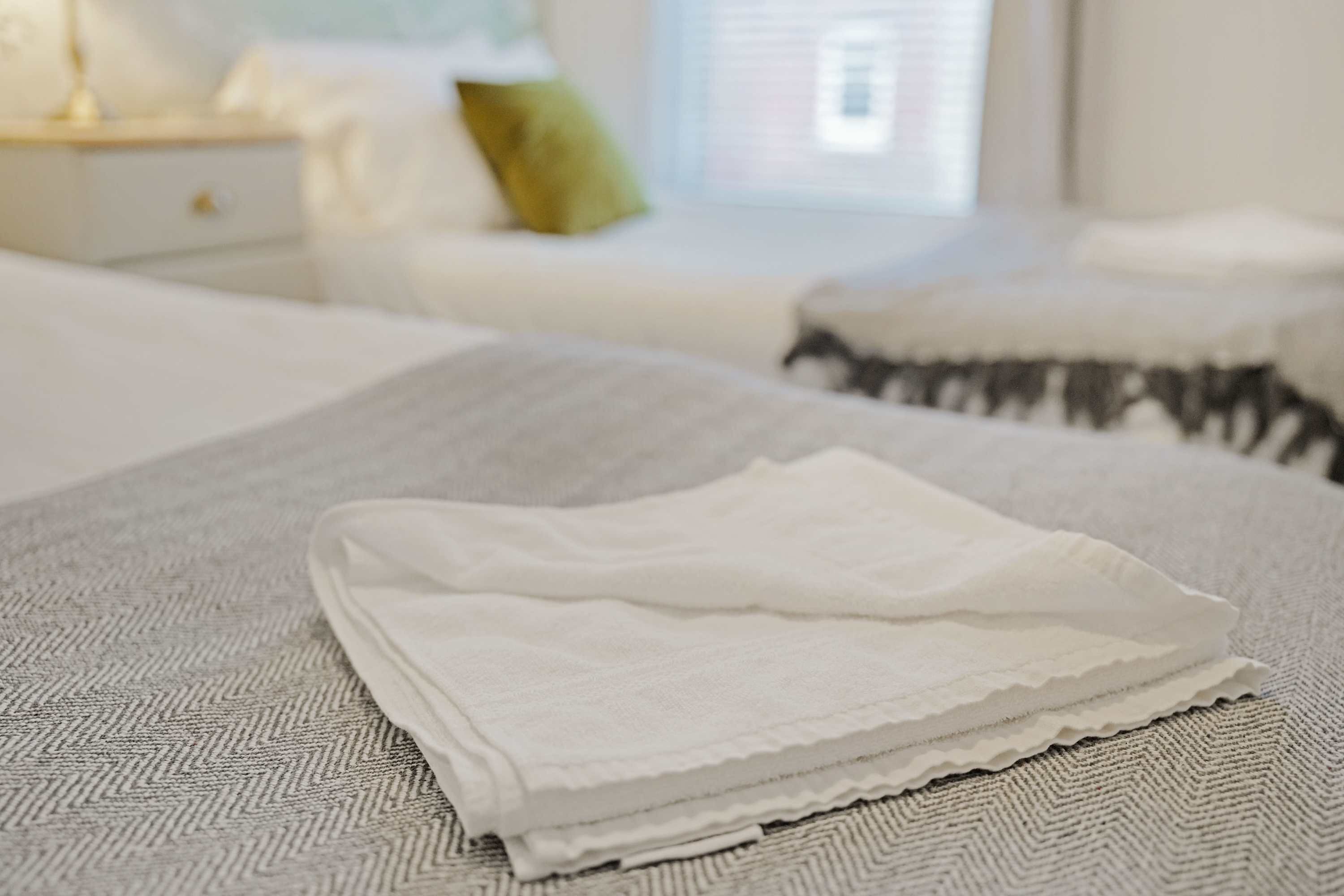 A neatly made bed with a folded white blanket in a room with a patterned carpet.