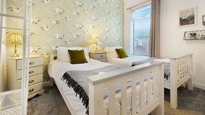 Ein Schlafzimmer mit einem Doppelbett, zwei Nachttischen mit Lampen, einem Fenster mit Jalousien und einer Wand mit Vogelmotiv.