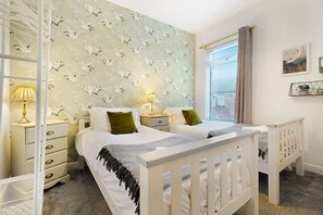 A bedroom with a double bed, two bedside tables with lamps, a window with blinds, and a wall with a bird pattern. - Coastal 3-bed Home for Families Contractors (Redcar)