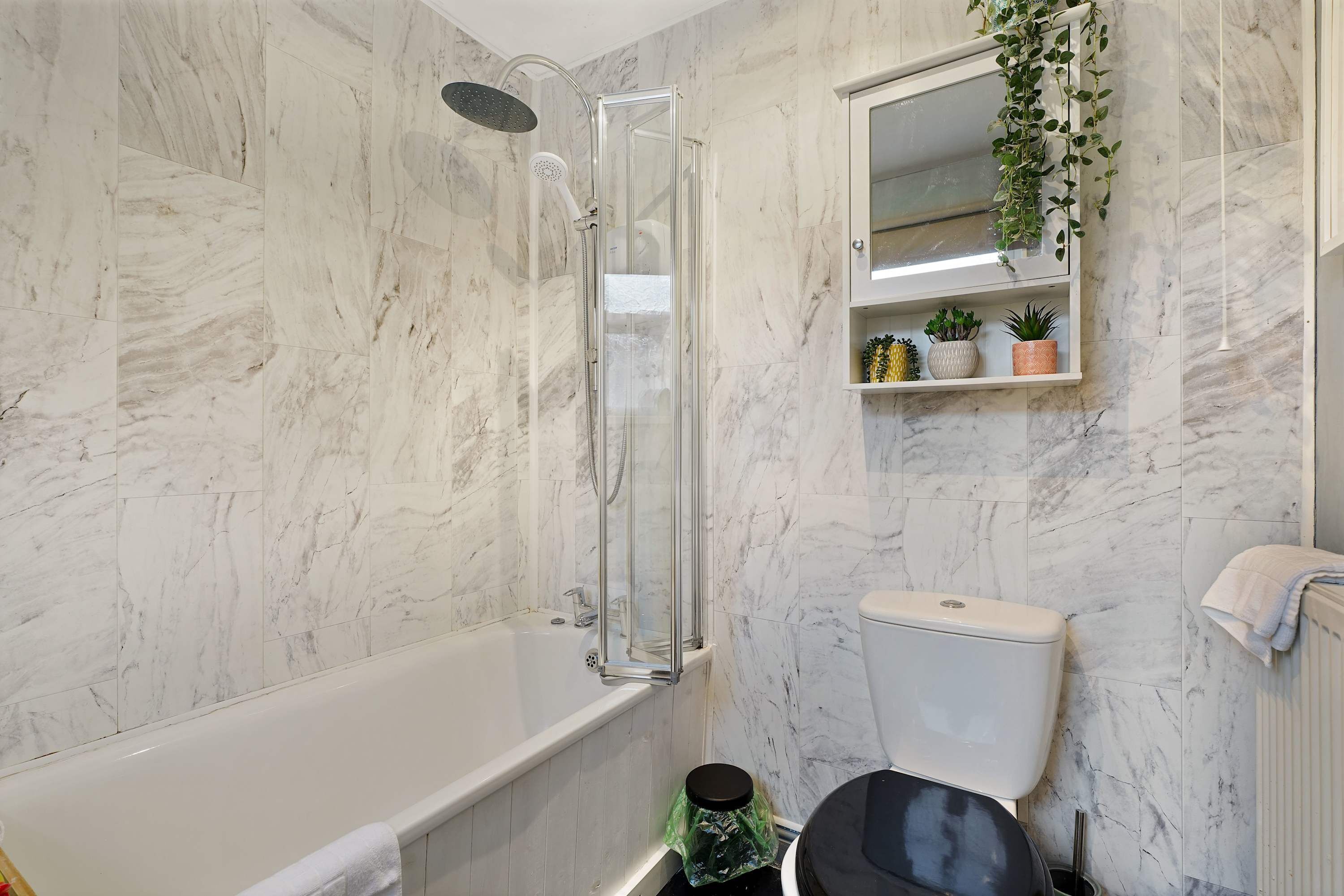 Ein Badezimmer mit einer gläsernen Duschkabine, einer Toilette und einem Pflanzenregal.