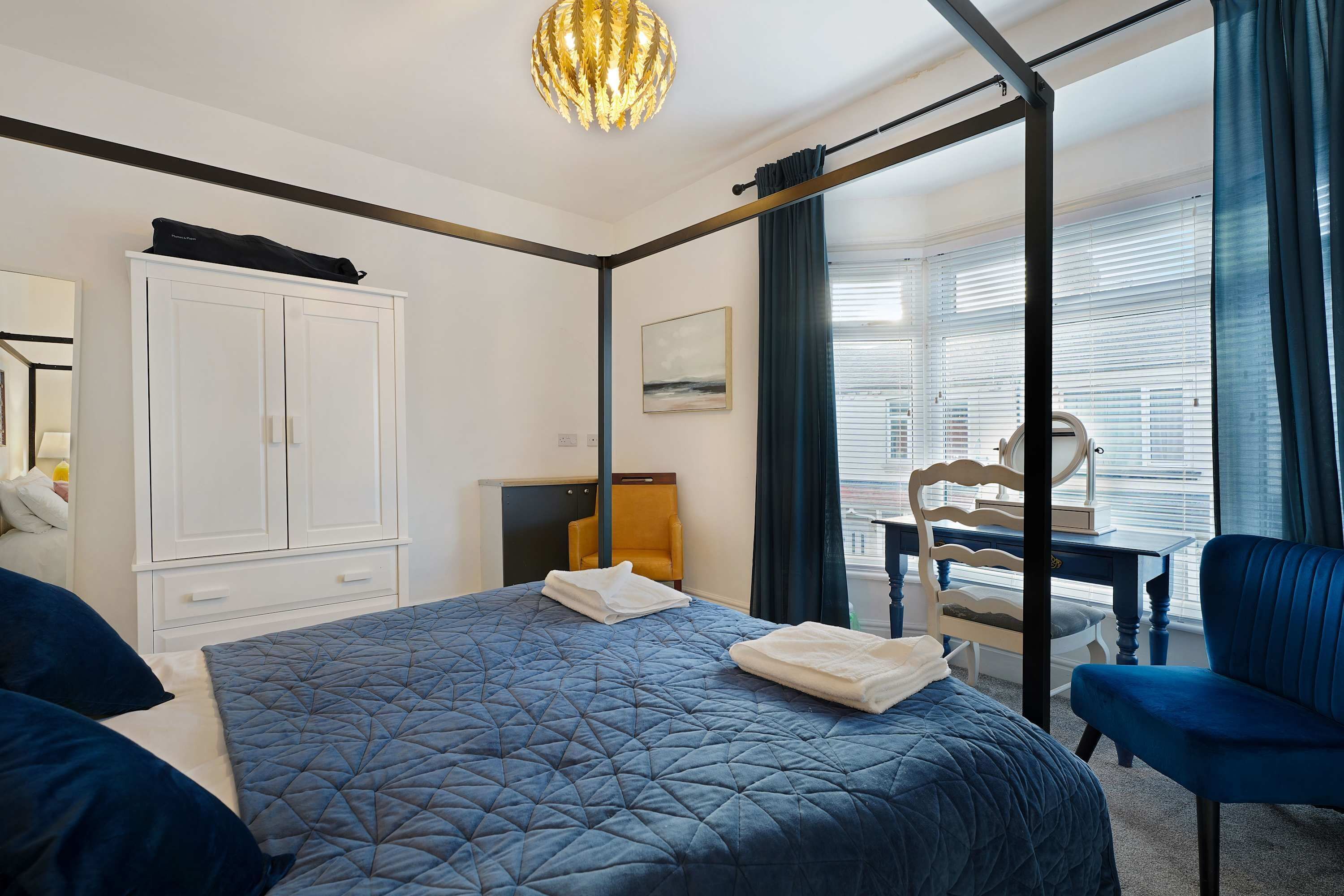 A hotel room with a large bed, a wardrobe, a desk, a chair, and a window with blinds.