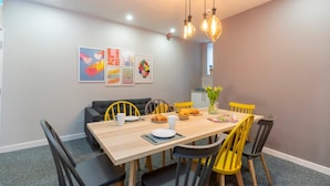 A dining area with a wooden table, yellow chairs, black benches, and a modern chandelier.