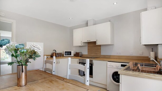 A modern kitchen with white cabinetry, a wooden countertop, and a dining table. - Duplex Apartment Close to A1 Private car Park (Darlington)