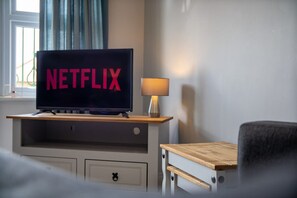 Ein Fernsehgerät auf einem Holzboden mit dem Schriftzug 'NETFLIX' auf dem Bildschirm, eine Lampe und ein Sessel.