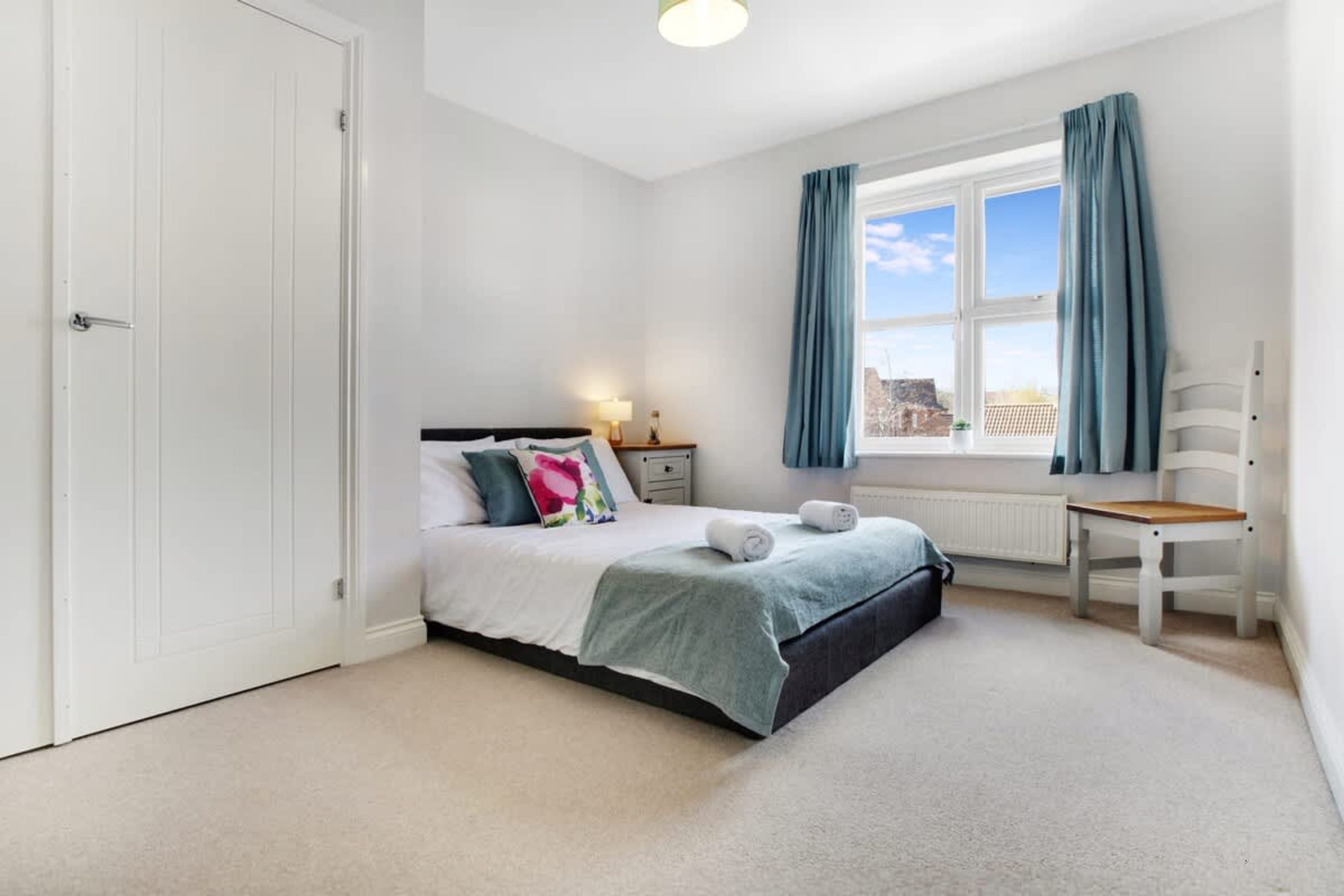A bedroom with a bed, a chair, a window with curtains, and a radiator.