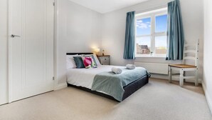 A bedroom with a bed, a chair, a window with curtains, and a radiator. - Duplex Apartment Close to A1 Private car Park (Darlington)