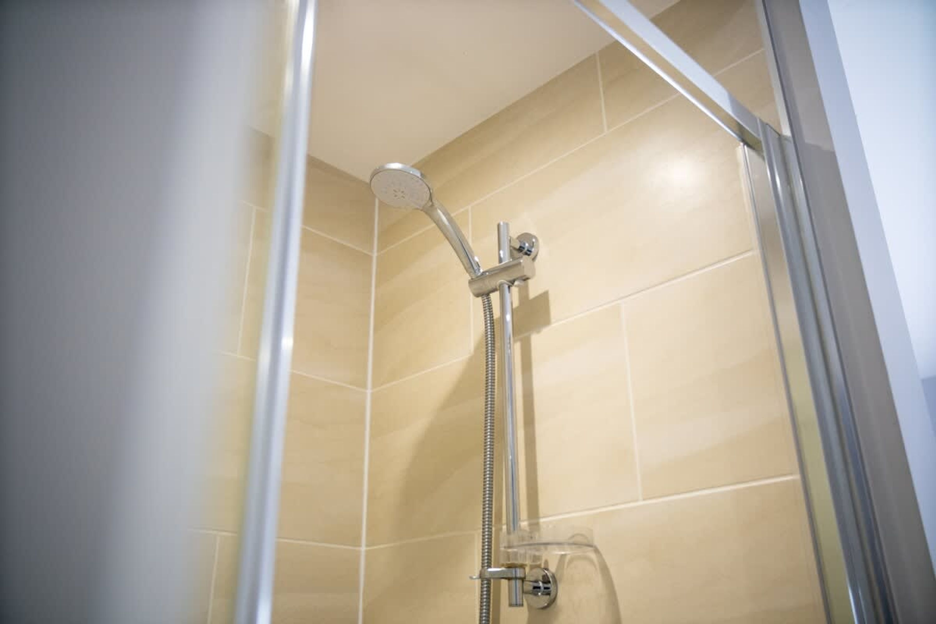 Een douche met een handdouche en een vastzitende kraan aan de muur.