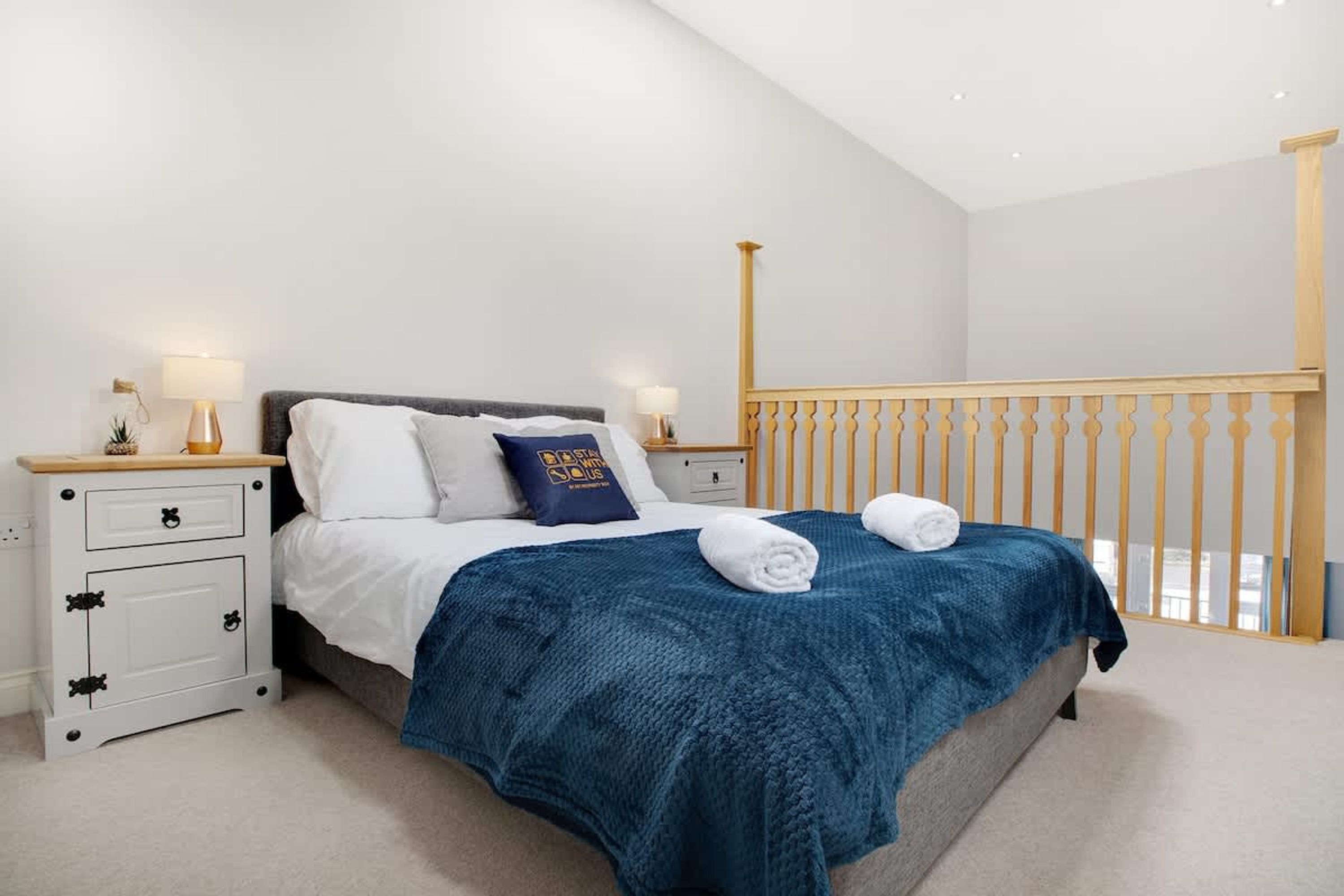 A bedroom with a bed, nightstands, a wooden railing, and a view of the outdoors.