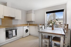 Una cocina moderna con armarios blancos, lavadora integrada y un comedor con mesa y sillas.