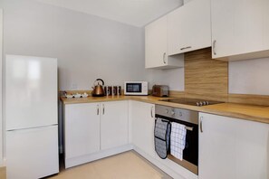 A modern kitchen with white cabinets, a wooden countertop, a stainless steel refrigerator, a microwave, a kettle, and a built-in oven. - Duplex Apartment Close to A1 Private car Park (Darlington)