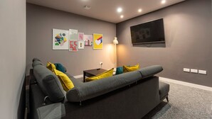 A modern living room with a grey sofa, colorful cushions, a flat-screen TV, and wall art.