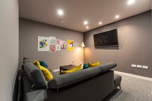 A modern living room with a grey sofa, colorful cushions, a flat-screen TV, and wall art.