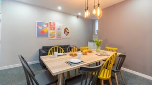 A dining area with a wooden table, yellow chairs, black benches, and a modern chandelier.
