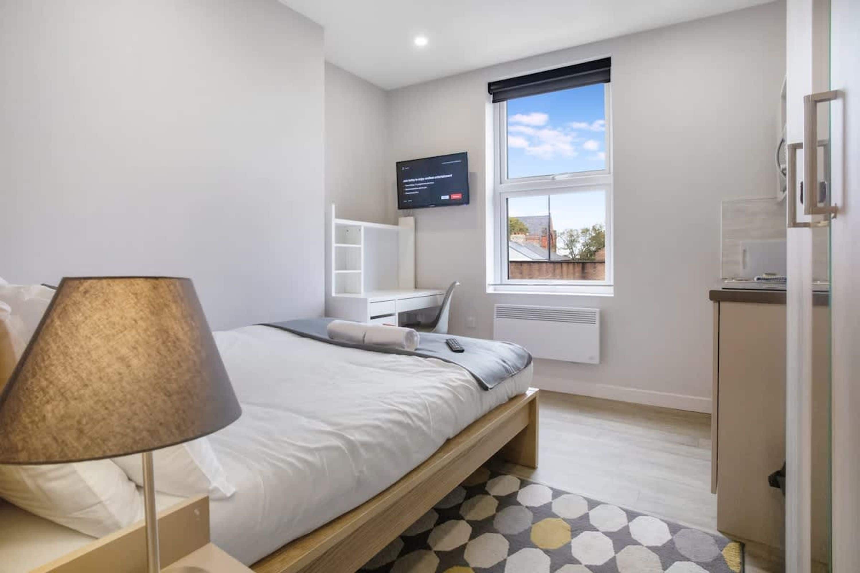 A bedroom with a bed, a desk, a TV, and a window with a view.