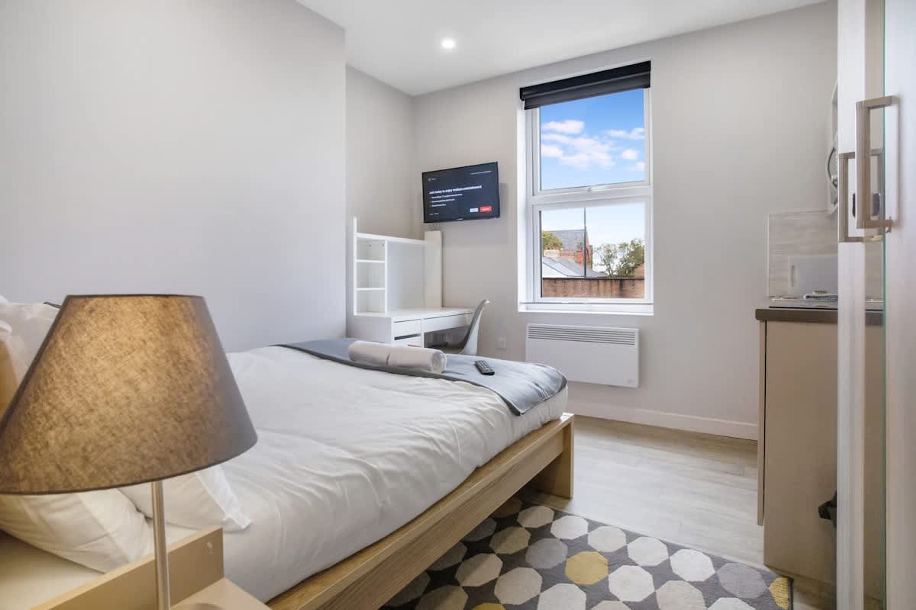 A bedroom with a bed, a desk, a TV, and a window with a view.