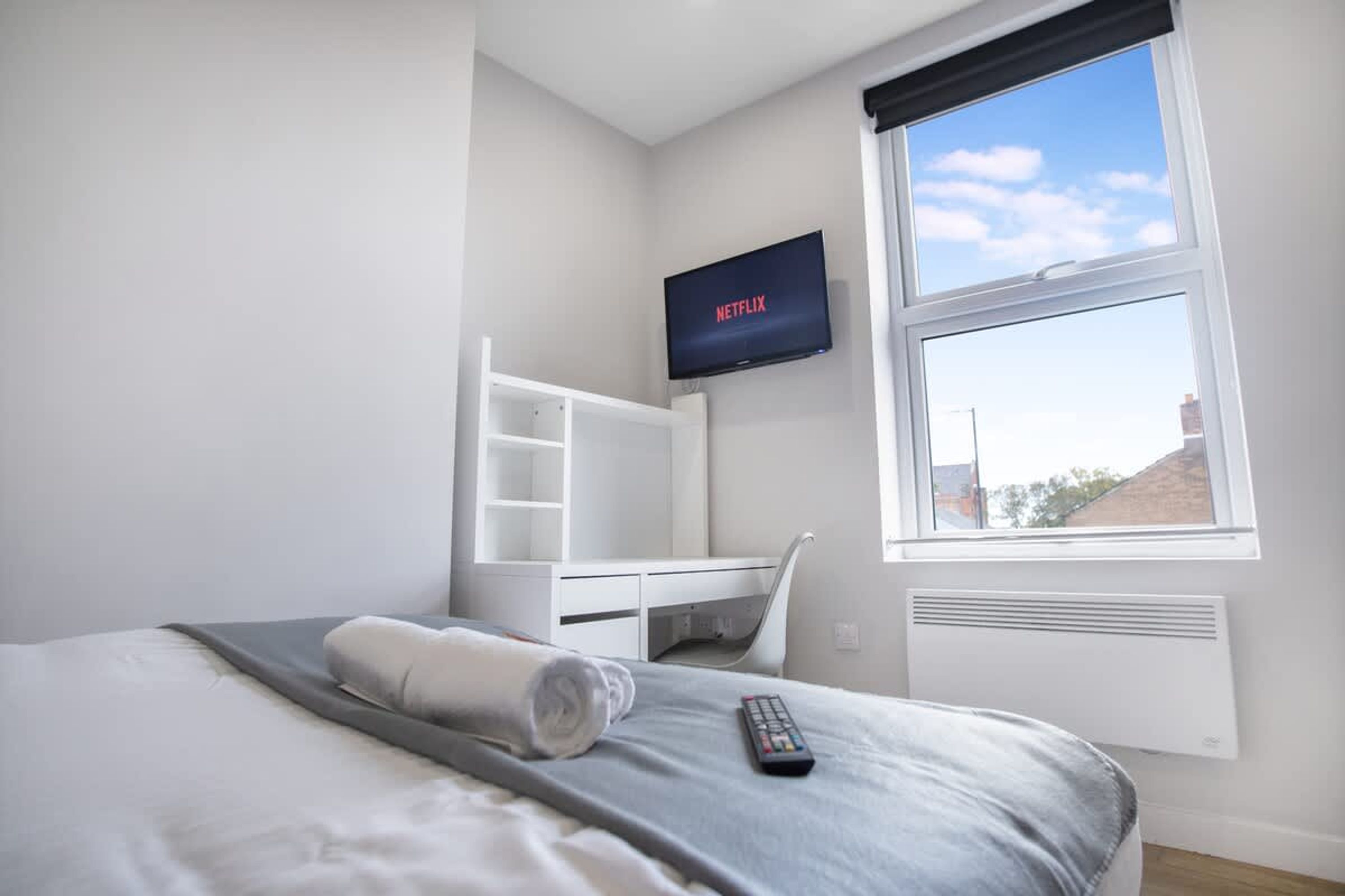 A hotel room with a bed, a TV mounted on the wall, a window with a view, and a white desk with shelves.