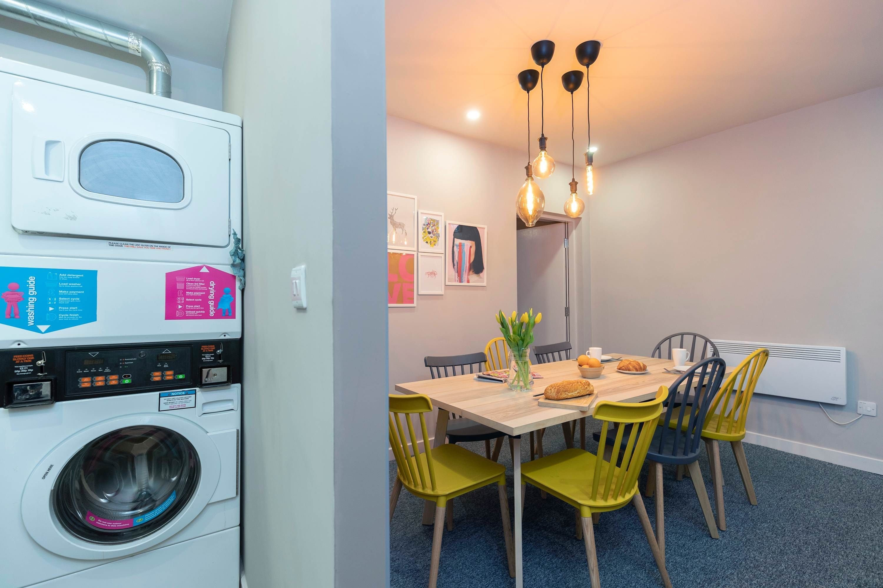 A compact kitchen with a washing machine, a dining table with chairs, and a hanging light fixture.