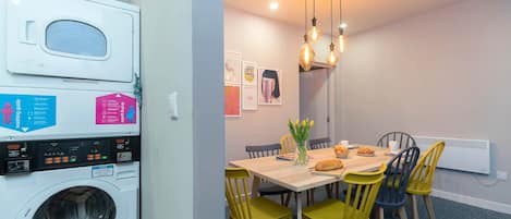 A compact kitchen with a washing machine, a dining table with chairs, and a hanging light fixture.