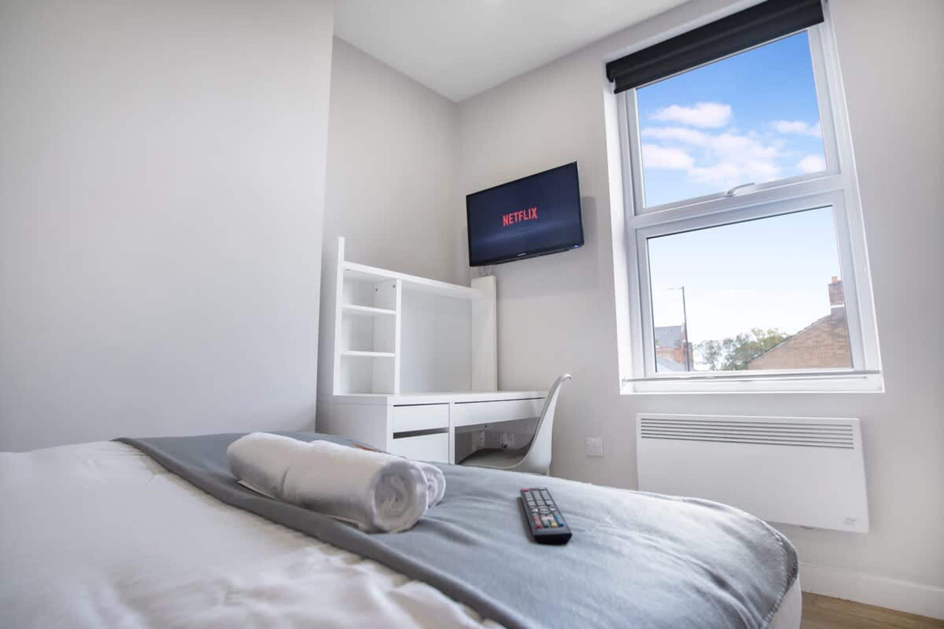 A hotel room with a bed, a TV mounted on the wall, a window with a view, and a white desk with shelves.