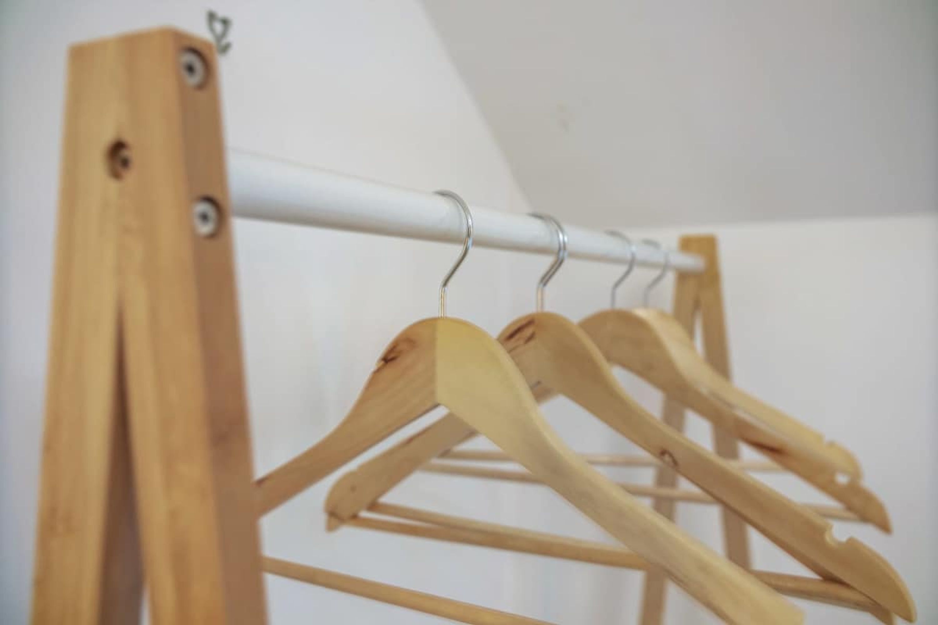 Ein hölzerner Kleiderständer mit mehreren Kleiderbügeln vor einer schlichten Wand.