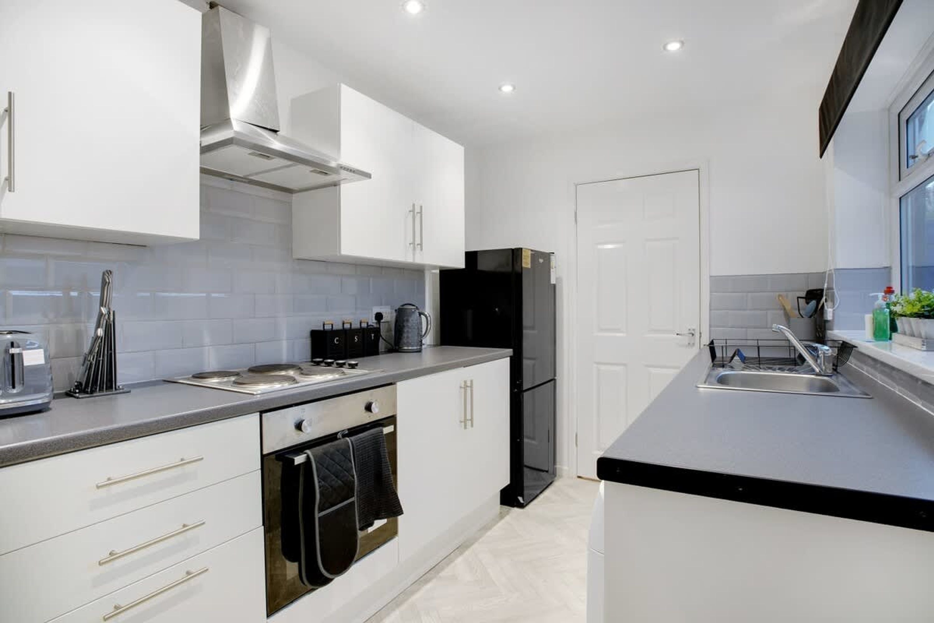 A modern kitchen with white cabinetry, a black refrigerator, and a stainless steel sink.