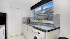A compact kitchen with a washing machine, a sink, and a window with a view. - Family two Bedroom Home Free Parking and Backyard (Crook)