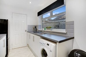 A compact kitchen with a washing machine, a sink, and a window with a view. - Family two Bedroom Home Free Parking and Backyard (Crook)
