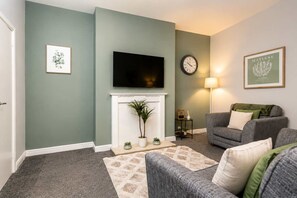 A living room with a fireplace, a television mounted above it, a clock on the wall, and a sofa. - Modern 2 Bed Near Seafront and Easy Commute Links (South Shields)