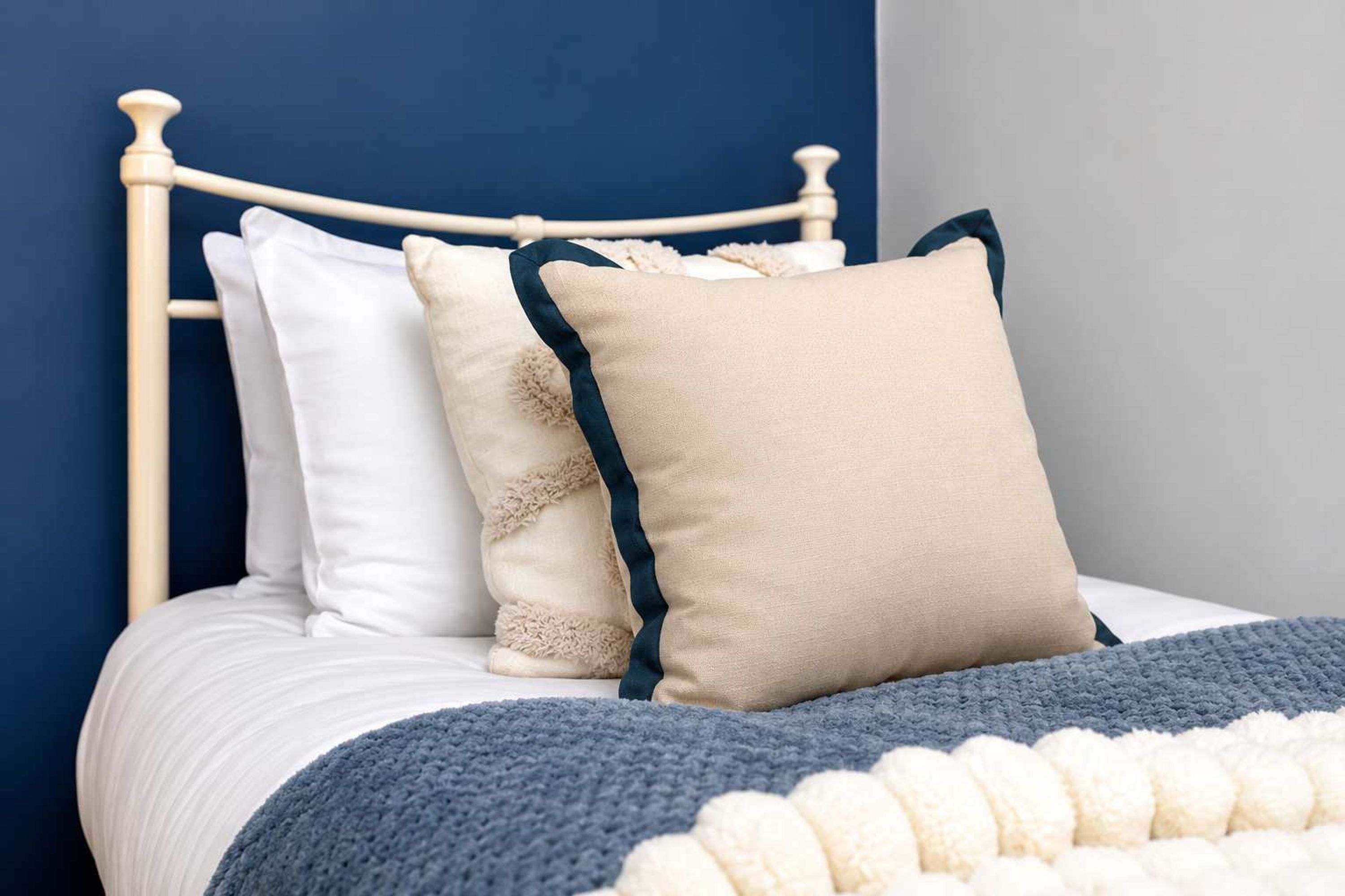 A bed with white bedding, two pillows with dark trim, and a blue knitted throw.