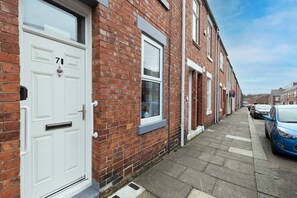 A residential street with a row of terraced houses, a white front door with the number 71, and parked cars. - Modern 2 Bed Near Seafront and Easy Commute Links (South Shields)