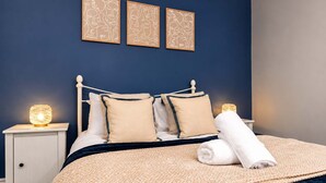 A neatly made bed with a dark blue headboard, two bedside tables with lamps, and three framed wall art pieces above the bed. - Modern 2 Bed Near Seafront and Easy Commute Links (South Shields)